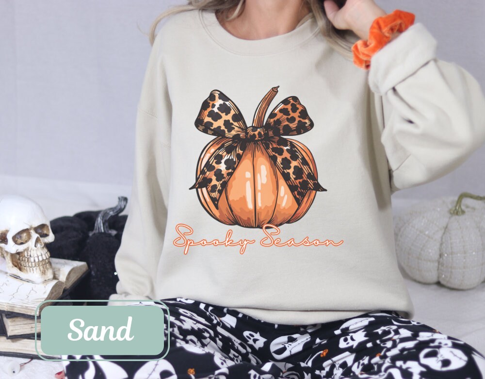 Sand-colored Halloween fall sweatshirt with "Spooky Season" pumpkin design and leopard bow. Perfect spooky shirt, and ghost crewneck. Ideal spooky sweatshirt for Halloween teacher or coquette clothing enthusiasts.