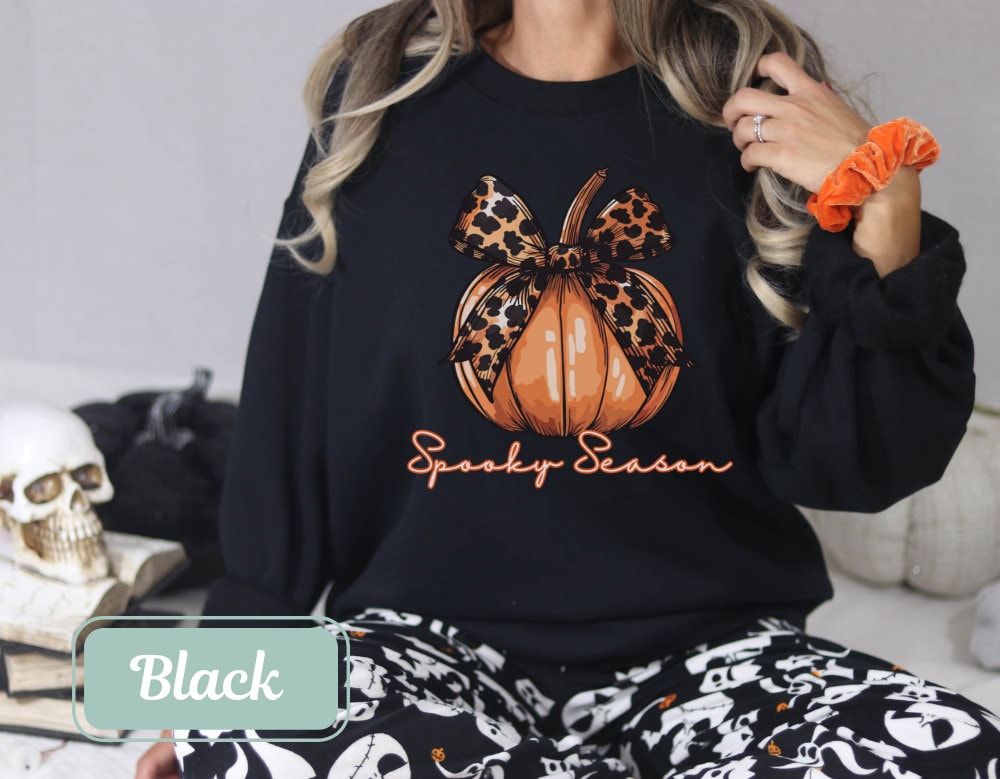 Black-colored Halloween fall sweatshirt with "Spooky Season" pumpkin design and leopard bow. Perfect spooky shirt, and ghost crewneck. Ideal spooky sweatshirt for Halloween teacher or coquette clothing enthusiasts.