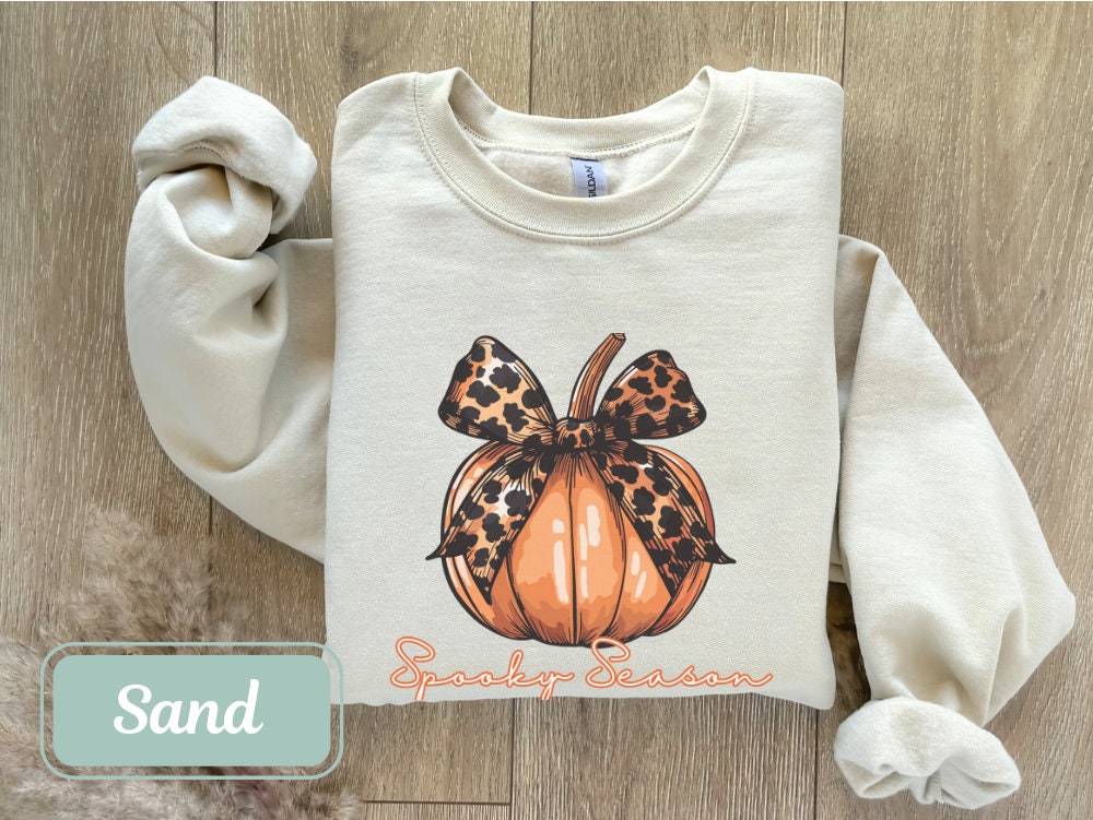 Sand-colored Halloween fall sweatshirt with "Spooky Season" pumpkin design and leopard bow. Perfect spooky shirt, and ghost crewneck. Ideal spooky sweatshirt for Halloween teacher or coquette clothing enthusiasts.