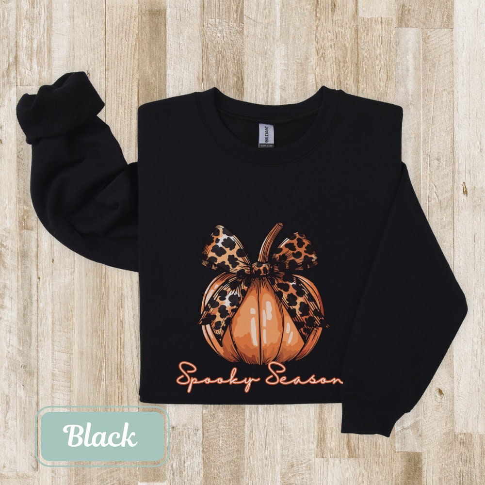 Black-colored Halloween fall sweatshirt with "Spooky Season" pumpkin design and leopard bow. Perfect spooky shirt, and ghost crewneck. Ideal spooky sweatshirt for Halloween teacher or coquette clothing enthusiasts.