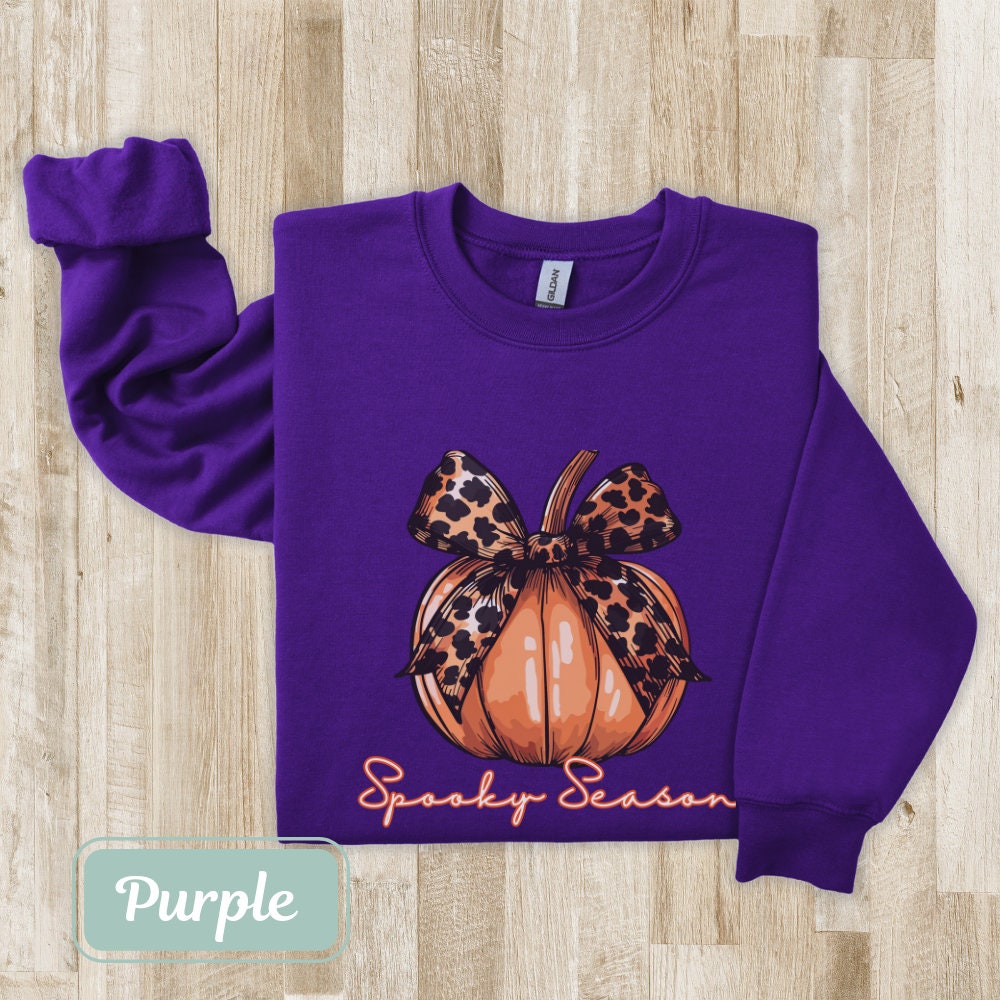 Purple-colored Halloween fall sweatshirt with "Spooky Season" pumpkin design and leopard bow. Perfect spooky shirt, and ghost crewneck. Ideal spooky sweatshirt for Halloween teacher or coquette clothing enthusiasts.
