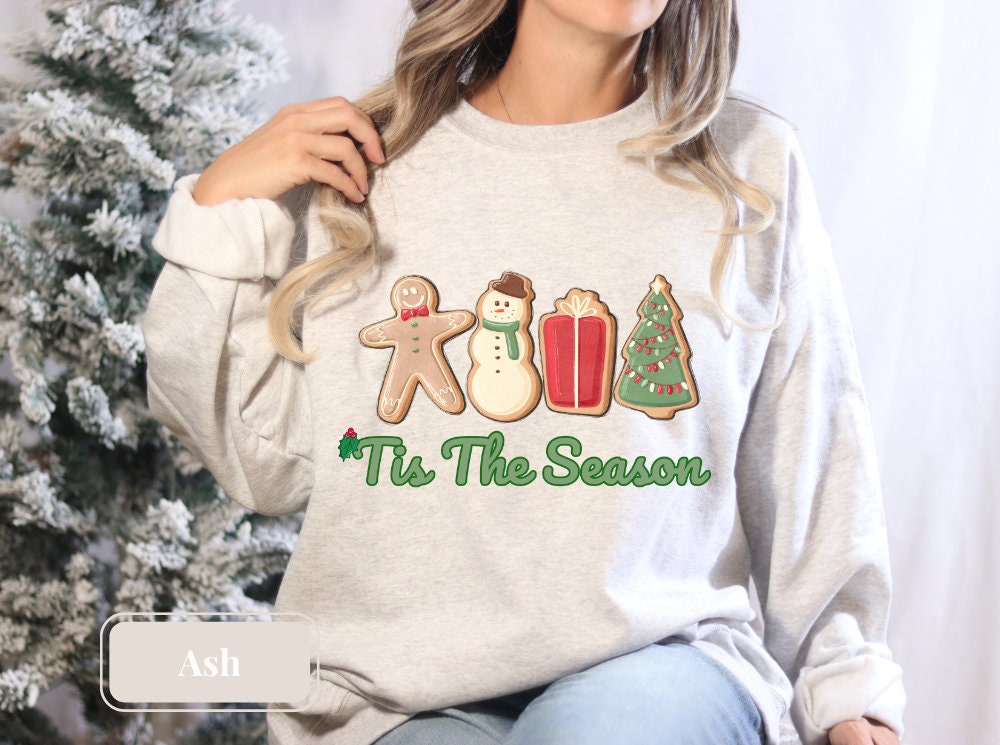 Ash holiday sweatshirt featuring gingerbread, snowman, present, and Christmas tree designs with 'Tis The Season' in green, perfect for Christmas lovers and cookie enthusiasts seeking a cozy winter shirt.
