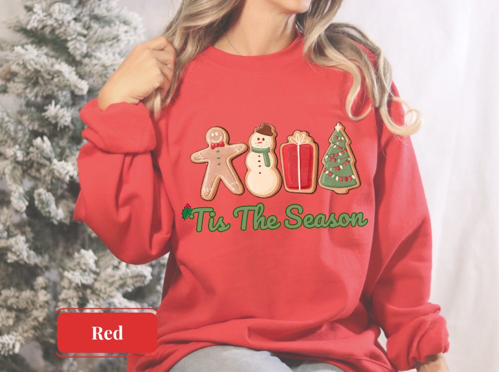 Bright red sweatshirt with gingerbread man, snowman, gift, and Christmas tree, featuring 'Tis The Season' in green. Ideal for merry and bright holiday celebrations, perfect for gingerbread lovers and festive gatherings.
