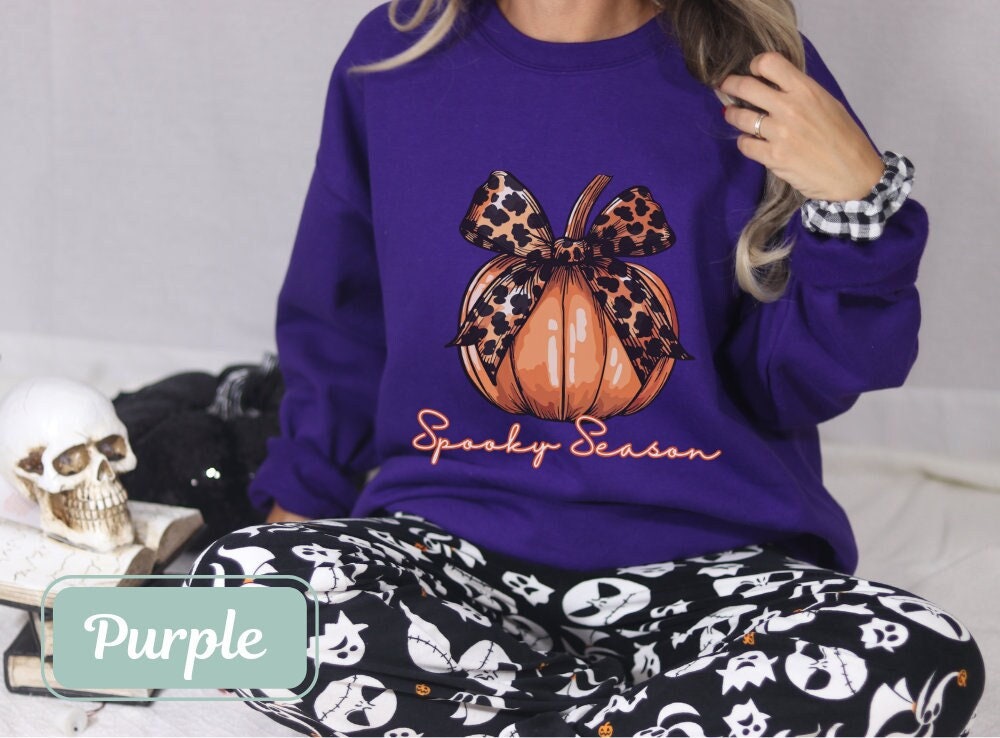Purple-colored Halloween fall sweatshirt with "Spooky Season" pumpkin design and leopard bow. Perfect spooky shirt, and ghost crewneck. Ideal spooky sweatshirt for Halloween teacher or coquette clothing enthusiasts.