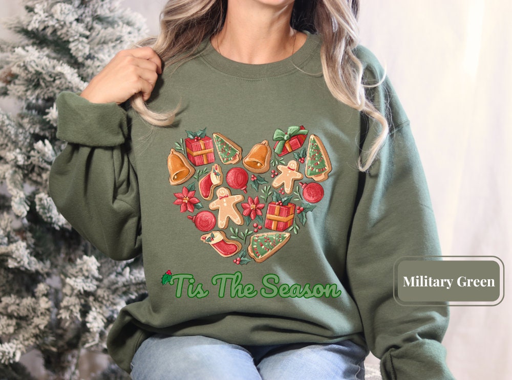 Military green holiday sweatshirt adorned with Christmas cookies, bells, and festive ornaments. Tagged as a Christmas tree shirt, this piece is perfect for gingerbread lovers and adds a touch of holiday spirit to any winter wardrobe.