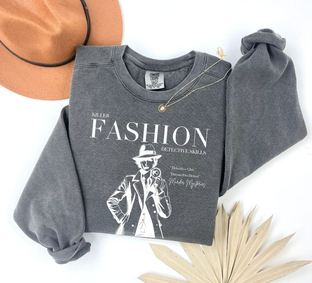 Pepper color sweatshirt folded with 'Killer Fashion Detective Skills' design in white. Ideal for true crime enthusiasts and fashion lovers. Makes a great gift for fans of murder mystery shows and podcasts.