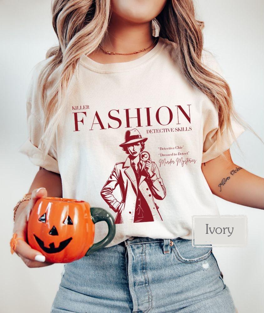 Ivory t-shirt with a bold red 'Killer Fashion Detective Skills' print. A must-have for true crime junkies, horror movie fans, and fashion-conscious crime show addicts. Perfect as a thoughtful gift or personal statement piece.