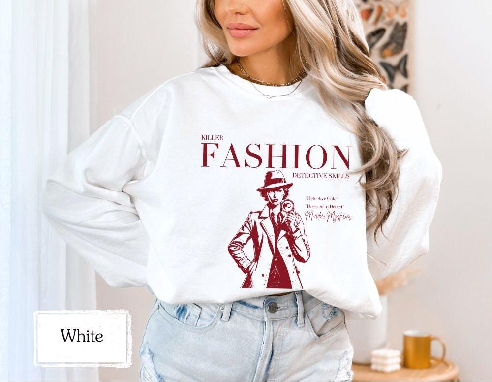 White sweatshirt with 'Killer Fashion Detective Skills' design in red, ideal for chilly days. Perfect for fans of true crime, murder shows, and detective stories. Cozy and stylish for casual wear or as a unique gift.