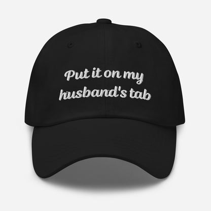 Close-up of a black dad hat featuring the embroidered text &#39;Put it on my husband&#39;s tab,&#39; highlighting the detailed stitching and practical design.