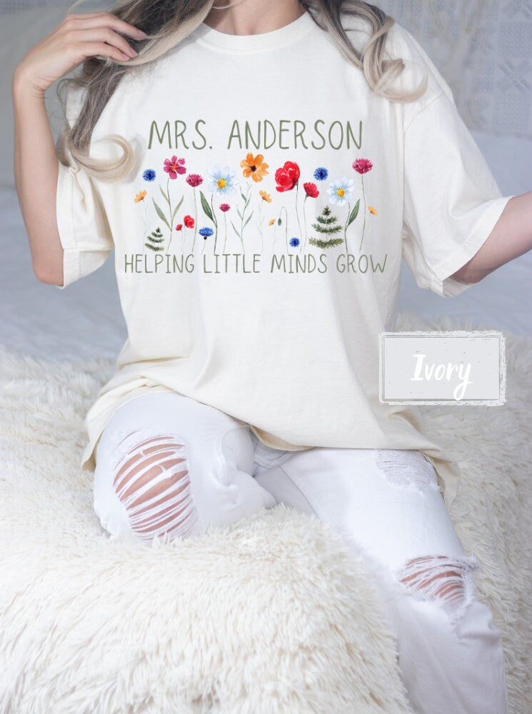 Elegant Ivory Comfort Colors teacher shirt, featuring &#39;Helping Little Minds Grow&#39; with a beautiful floral design. Customizable name and text color, ideal for teacher appreciation and new teacher gifts.