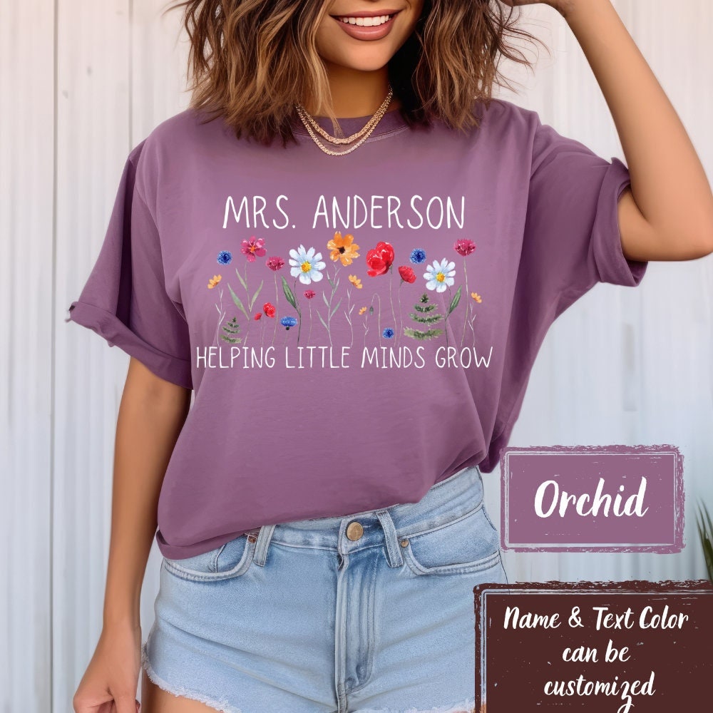 Comfort Colors Orchid teacher t-shirt with &#39;Helping Little Minds Grow&#39; and wildflowers design. Customizable name and text color. Ideal for kindergarten, first-grade teachers, and new teacher gifts.