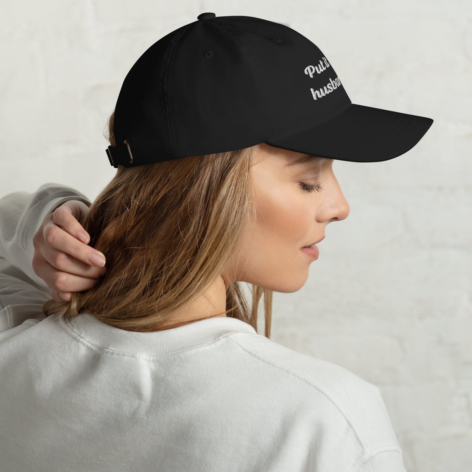 A side view of the classic black dad hat with &quot;Put it on my husband&#39;s tab&quot; embroidered. Great for dad, wife, or bride. Funny and sarcastic, a perfect vintage-style gift.