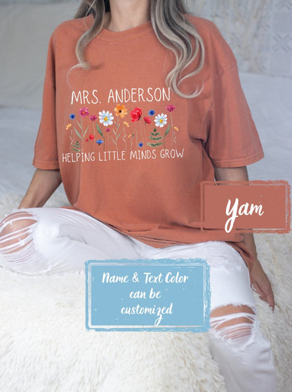 Yam colored Comfort Colors shirt personalized for teachers with &#39;Helping Little Minds Grow&#39; surrounded by colorful wildflowers. Ideal for first day of school, teacher shirts, and appreciation gifts.