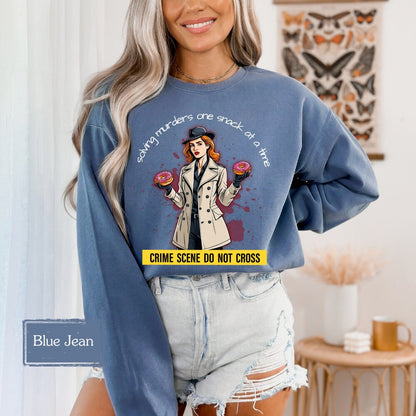 Blue Jean-colored sweatshirt with a funny murder mystery design, featuring a detective with donuts and the phrase &#39;solving murders one snack at a time.&#39; A cozy and stylish choice for crime show fans and snack lovers alike.