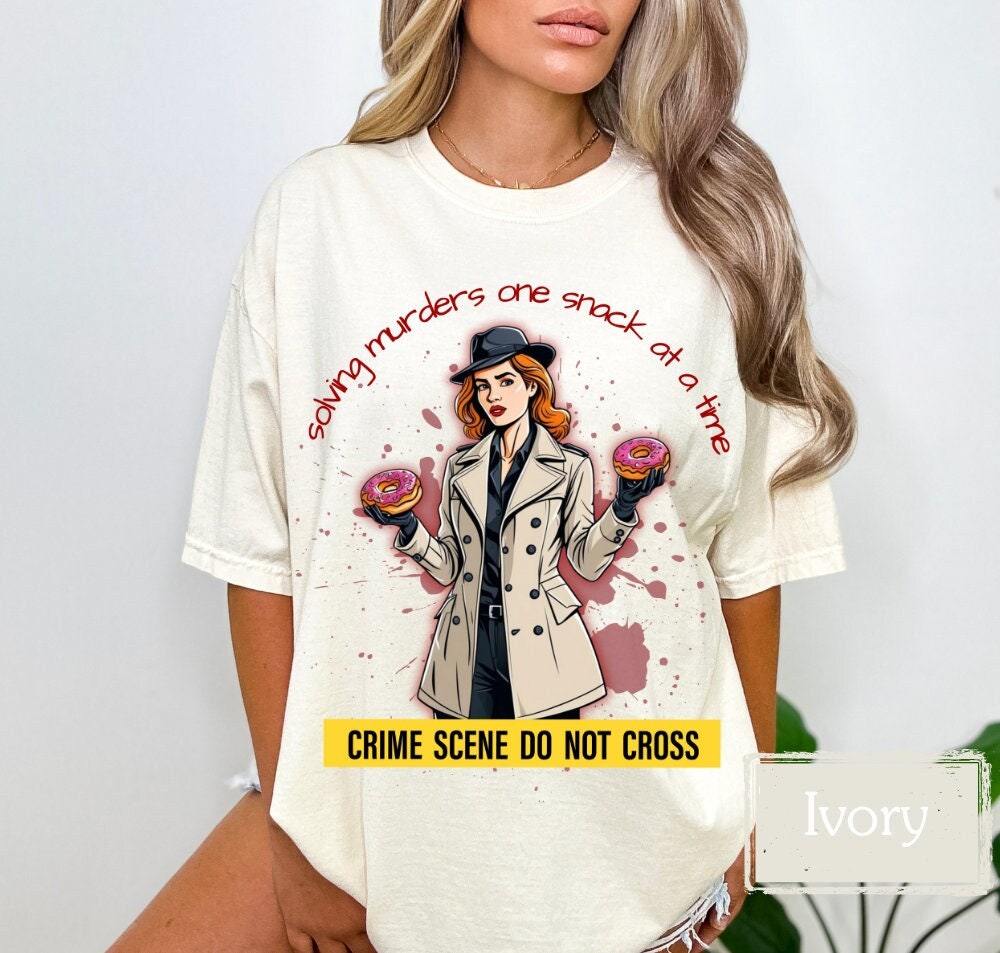 Ivory shirt with a funny &#39;Murder Mystery&#39; theme, featuring a detective holding donuts and the slogan &#39;solving murders one snack at a time.&#39; Perfect for crime junkies, snack lovers, and true crime fans. Great gift for murder mystery enthusiasts.