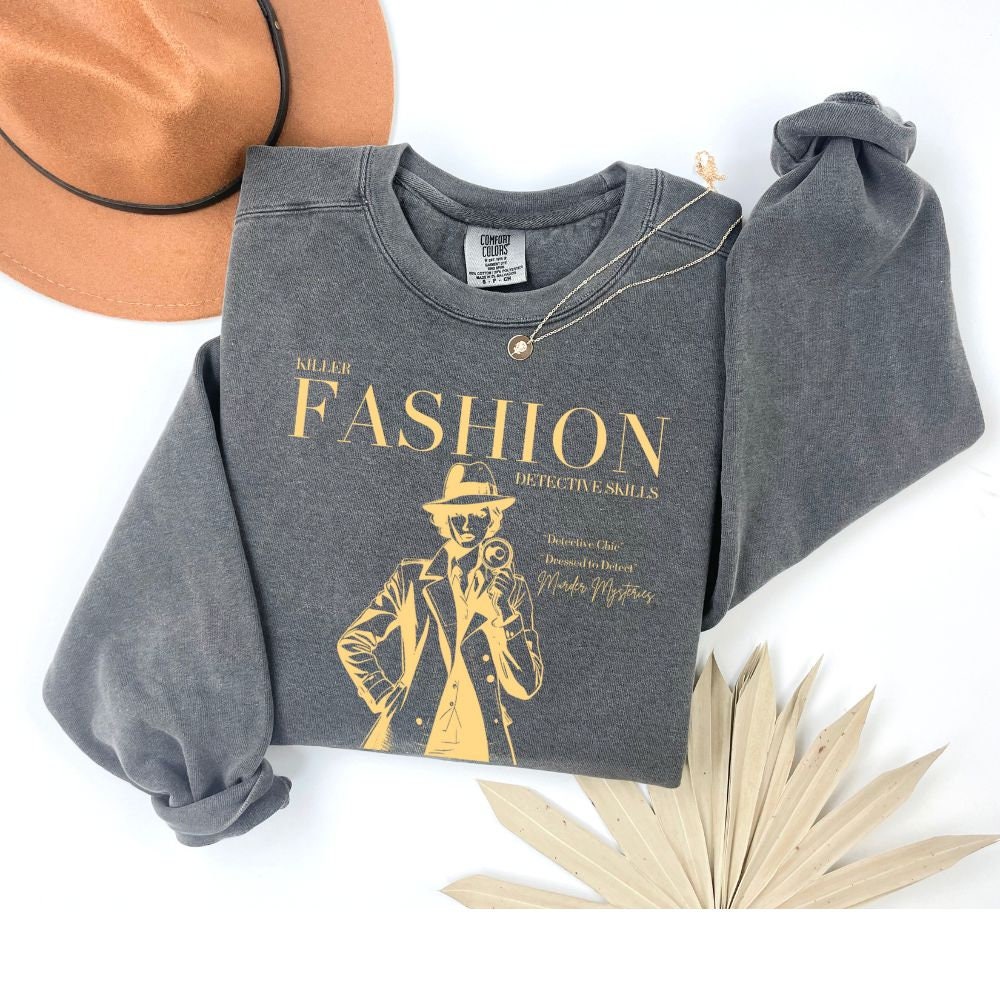 Pepper color sweatshirt folded with &#39;Killer Fashion Detective Skills&#39; design in gold. Ideal for true crime enthusiasts and fashion lovers. Makes a great gift for fans of murder mystery shows and podcasts.