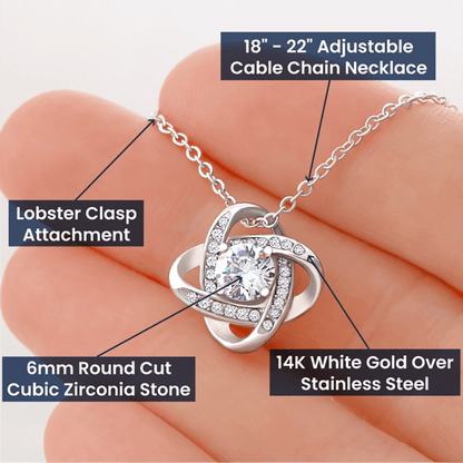 Close-up of a hand displaying a 14K White Gold Over Stainless Steel Love Knot Necklace with a 6mm Round Cut Cubic Zirconia Stone and Lobster Clasp Attachment on an 18”-22” Adjustable Cable Chain.
