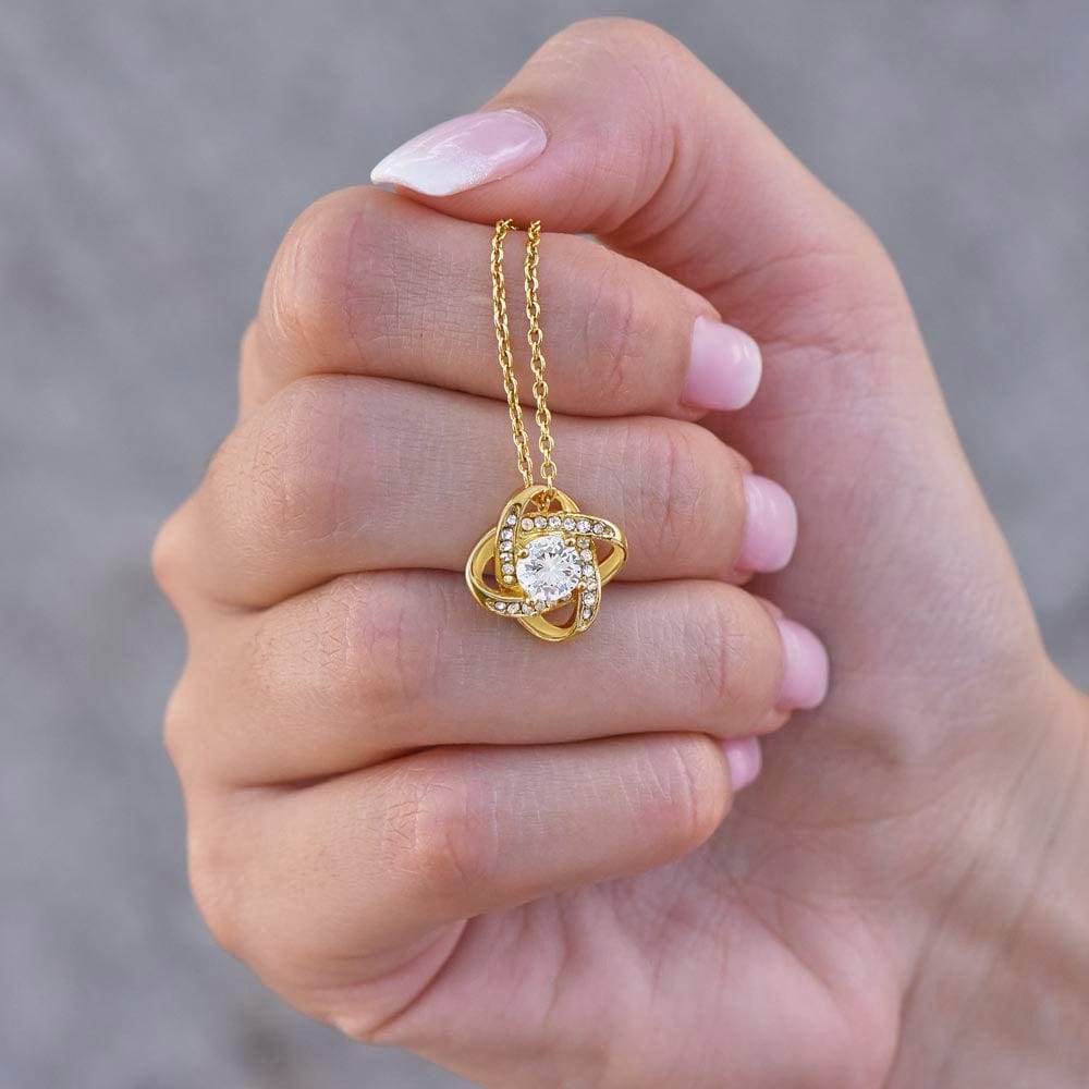 Gentle hand clutching a Gold Love Knot Necklace with Cubic Zirconia - a meaningful and elegant jewelry gift for daughters from their fathers, highlighted against a soft-focus background.